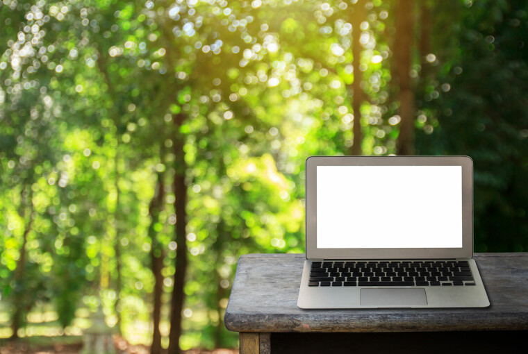 En bærbar PC på en trebenk utendørs med skog i bakgrunnen